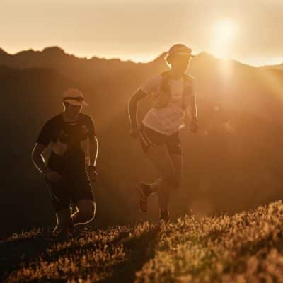 FP Events | Switzerland Tourism / Colin Frei, Une femme et un homme faisant du trail dans les montagnes au lever du soleil.